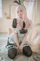 A woman with long pink hair sitting on a bed.