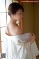 A woman in a white dress standing by a window.