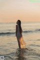 A woman standing in the ocean at sunset.