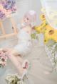 A woman in a white dress sitting on a white rug next to flowers.