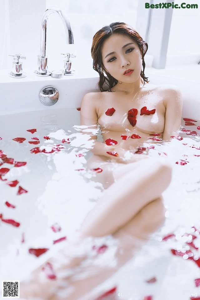 A woman sitting in a bathtub filled with rose petals.