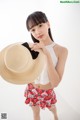 A woman in a white top and red skirt holding a straw hat.