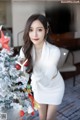 a woman in a white dress standing next to a christmas tree