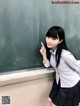 A young woman in a school uniform pointing at a blackboard.