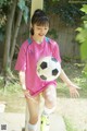 A young girl in a pink shirt kicking a soccer ball.